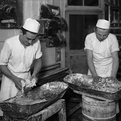 Christstollenbäckerei. Backstube. Dem Stollenteigs werden die Zutaten (Mandeln, Rosinen, Zitronat, etc.) mit der Hand beigemischt